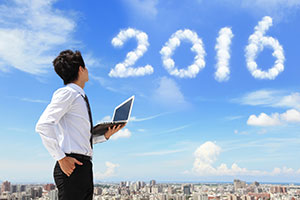 Businessman holding a tablet while looking at "2016" written in cloud numbers against a blue sky.