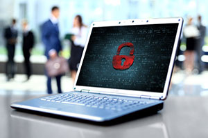 A laptop displaying a red padlock icon on screen, symbolizing cybersecurity, with blurred people in the background.